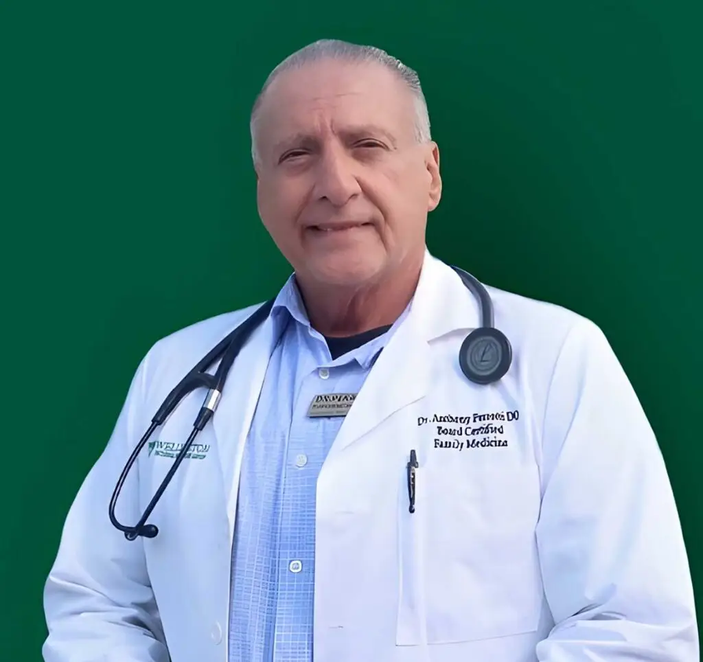 Older doctor in white coat with stethoscope smiling against green background