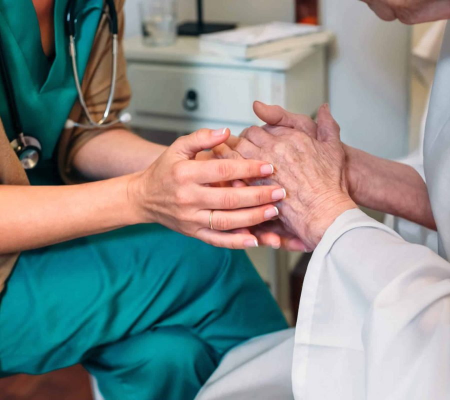 Female doctor giving encouragement to elderly patient by holding her hands