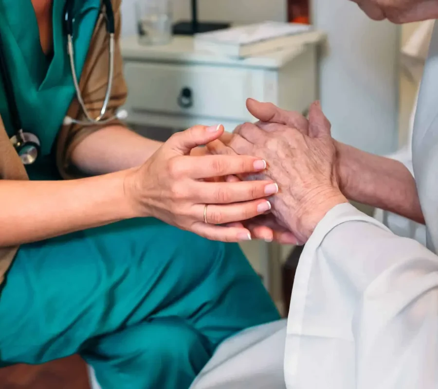 Doctor comforting patient by gently holding hands during healthcare consultation